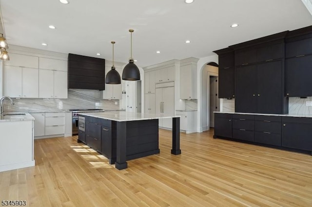 kitchen with a kitchen island, backsplash, arched walkways, a sink, and stainless steel range oven
