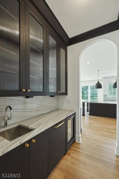 bar with crown molding, light wood-type flooring, arched walkways, a sink, and decorative light fixtures