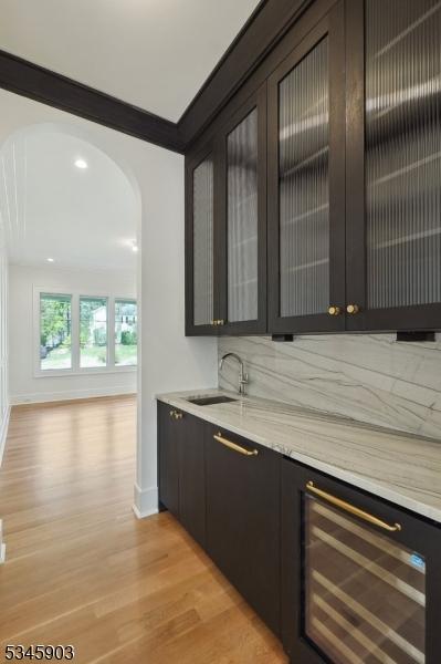 bar with a sink, light wood-style floors, beverage cooler, arched walkways, and baseboards