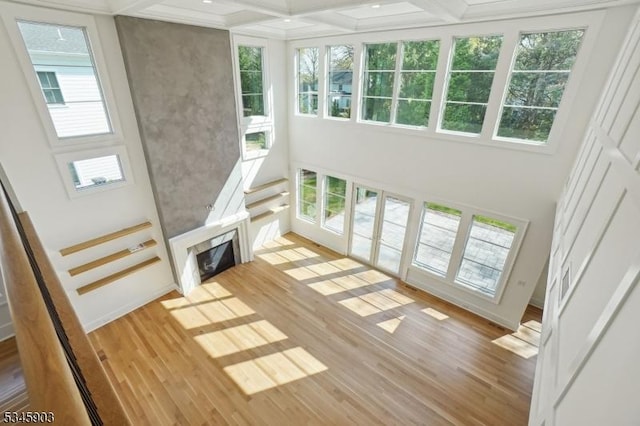 unfurnished living room with plenty of natural light, beamed ceiling, coffered ceiling, and light wood-type flooring