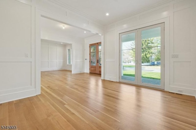 interior space featuring ornamental molding, a decorative wall, light wood-style floors, recessed lighting, and french doors