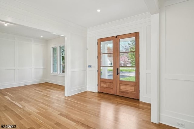 doorway with crown molding, french doors, light wood-style flooring, and a decorative wall