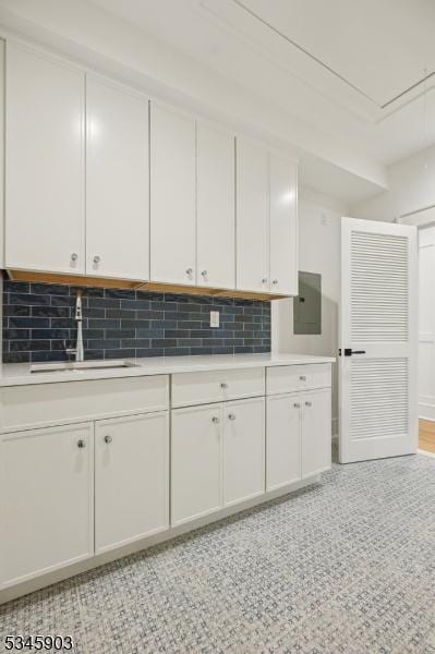 kitchen with light countertops, white cabinetry, electric panel, tasteful backsplash, and a sink