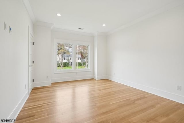 empty room featuring baseboards, visible vents, ornamental molding, and light wood finished floors