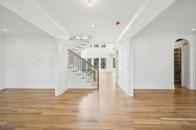 foyer with crown molding, a decorative wall, arched walkways, light wood-type flooring, and stairway