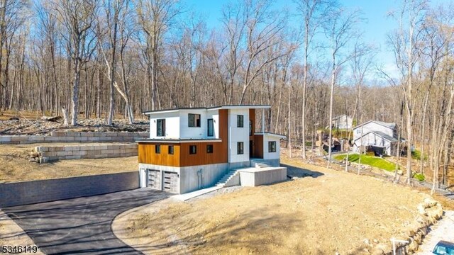 view of front of home featuring a garage, a forest view, driveway, and fence
