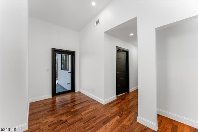 spare room with wood finished floors, visible vents, baseboards, and a high ceiling