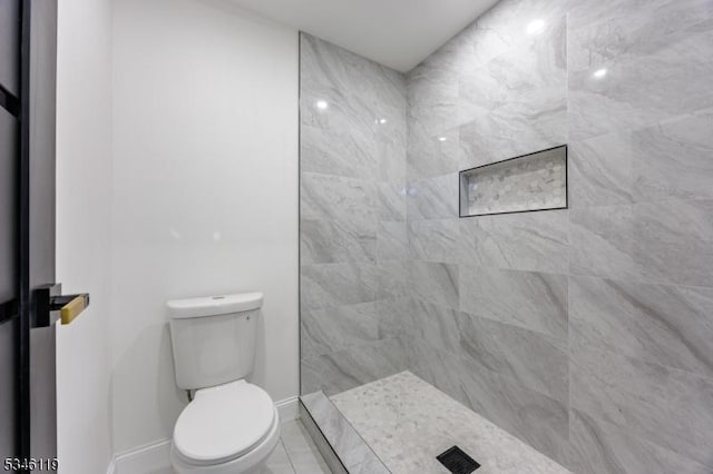 bathroom with toilet, baseboards, and tiled shower