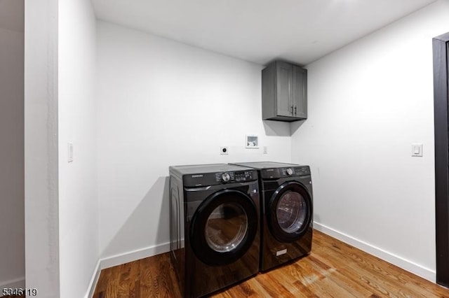 laundry area featuring washing machine and clothes dryer, baseboards, light wood-style floors, and cabinet space