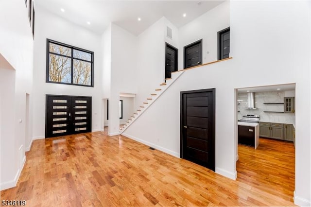 foyer with baseboards, a towering ceiling, light wood-style floors, and stairway
