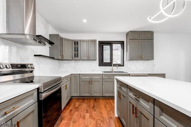 kitchen with wall chimney range hood, a sink, decorative backsplash, stainless steel range with electric stovetop, and light countertops