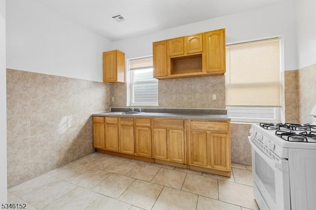 kitchen featuring tile walls, light tile patterned flooring, a sink, visible vents, and white range with gas stovetop
