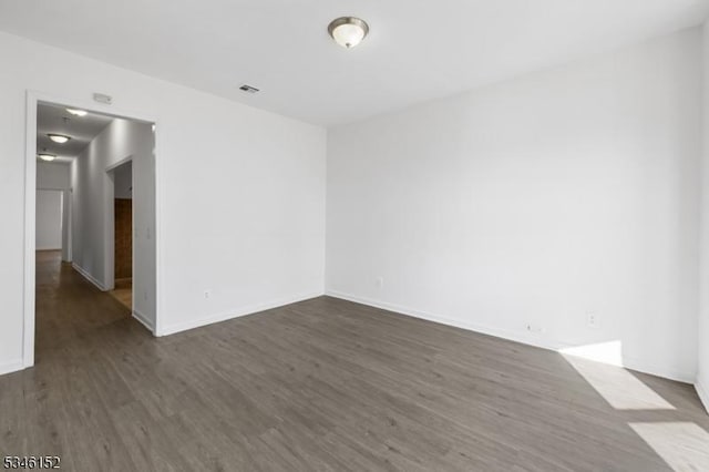 empty room with dark wood-style floors, visible vents, and baseboards
