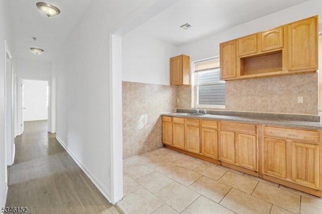kitchen with light tile patterned flooring, a sink, light brown cabinetry, visible vents, and tile walls