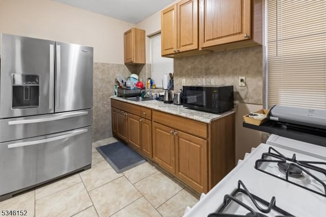 kitchen with tile walls, brown cabinets, black microwave, stainless steel refrigerator with ice dispenser, and light tile patterned floors
