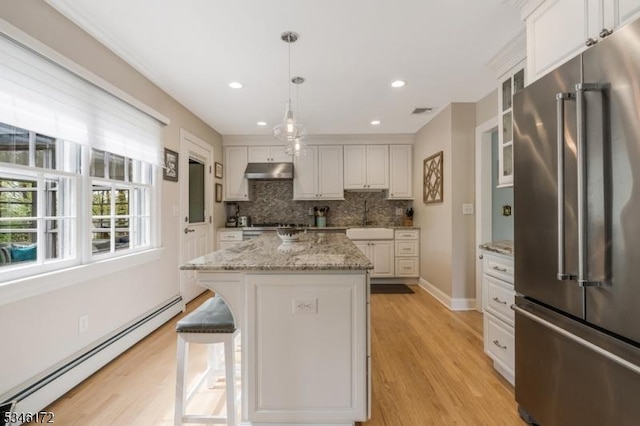 kitchen with baseboard heating, high quality fridge, backsplash, under cabinet range hood, and glass insert cabinets