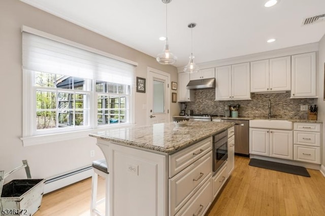 kitchen with a sink, light wood-style floors, tasteful backsplash, under cabinet range hood, and visible vents