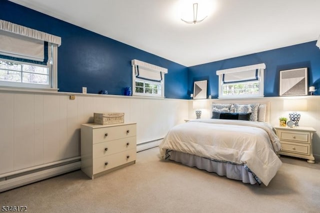 carpeted bedroom featuring wainscoting, baseboard heating, and multiple windows