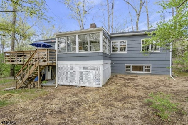 back of property with a deck, a chimney, stairs, and a sunroom