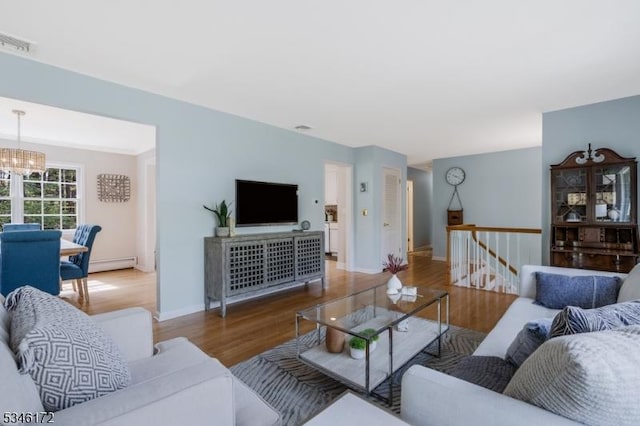 living room featuring visible vents, baseboard heating, wood finished floors, baseboards, and a chandelier