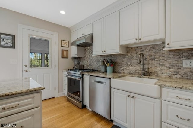 kitchen with decorative backsplash, a sink, white cabinets, under cabinet range hood, and stainless steel appliances
