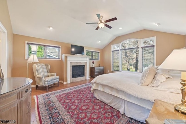 bedroom featuring multiple windows, wood finished floors, lofted ceiling, and a tile fireplace