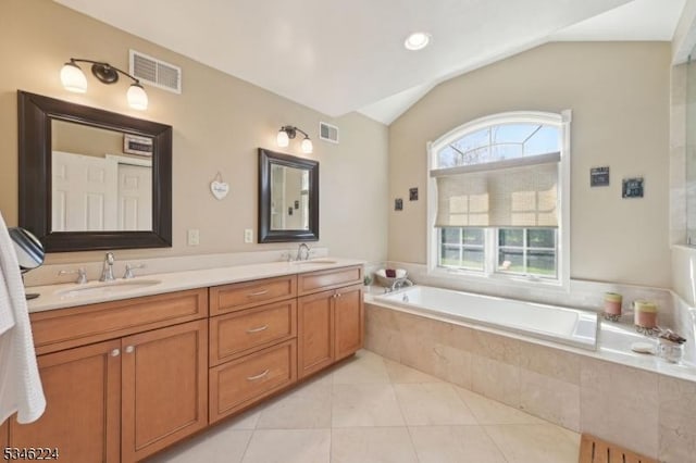 full bath with a sink, vaulted ceiling, tiled tub, and visible vents