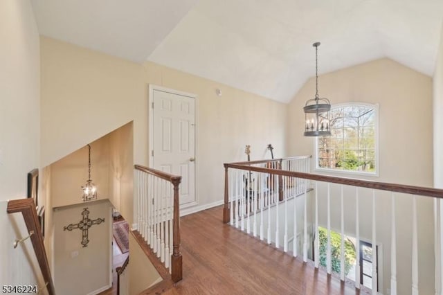 corridor with an inviting chandelier, lofted ceiling, wood finished floors, and an upstairs landing