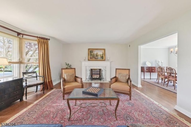 living room with a premium fireplace, baseboards, an inviting chandelier, and wood finished floors