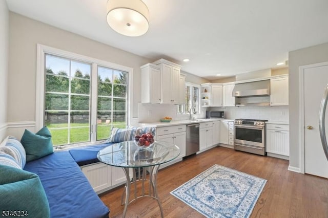 kitchen with appliances with stainless steel finishes, open shelves, white cabinetry, light countertops, and wall chimney exhaust hood
