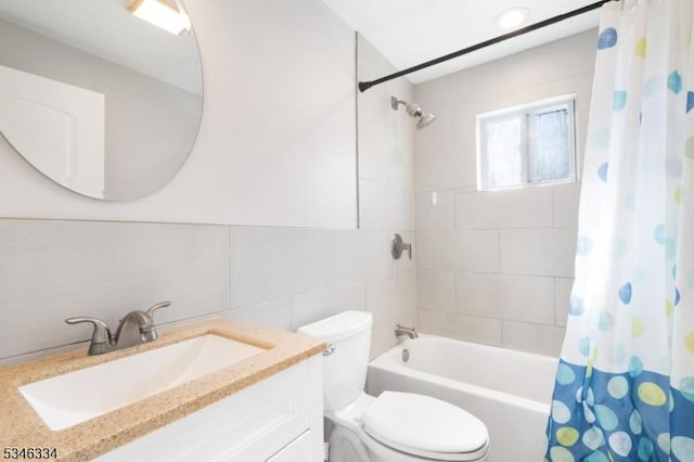 bathroom with shower / tub combo with curtain, toilet, vanity, and tile walls