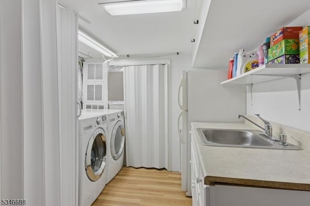 laundry area featuring independent washer and dryer, light wood finished floors, and a sink