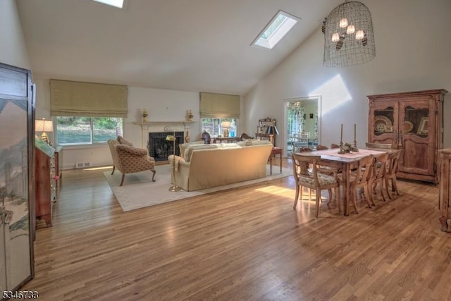 interior space with an inviting chandelier, a fireplace, high vaulted ceiling, wood finished floors, and a skylight
