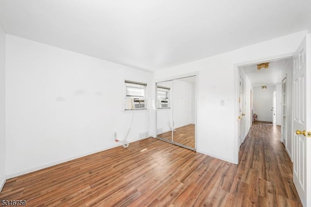 unfurnished bedroom featuring a closet, visible vents, light wood finished floors, baseboards, and cooling unit