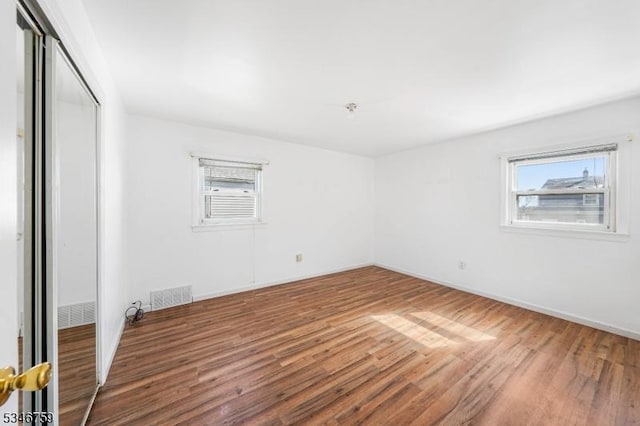unfurnished bedroom featuring wood finished floors, baseboards, a closet, and visible vents
