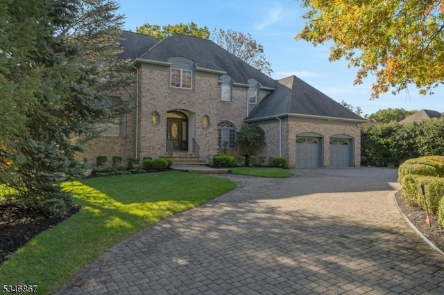 french provincial home featuring brick siding, a garage, a front yard, and decorative driveway