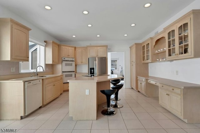 kitchen featuring light countertops, white appliances, light brown cabinets, a breakfast bar area, and a center island
