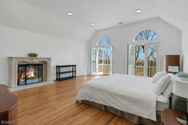 bedroom with vaulted ceiling, light wood finished floors, a fireplace, access to outside, and recessed lighting