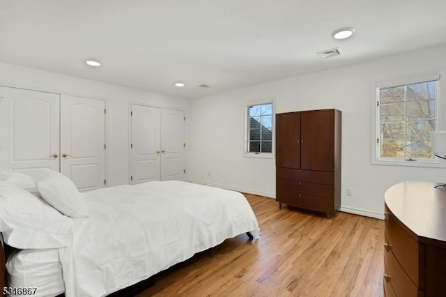 bedroom with multiple closets, visible vents, baseboards, recessed lighting, and light wood-style floors