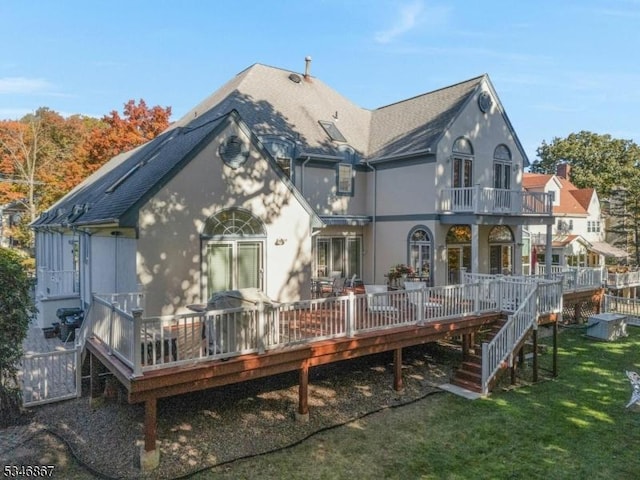 rear view of house with stucco siding, a shingled roof, a yard, and a balcony