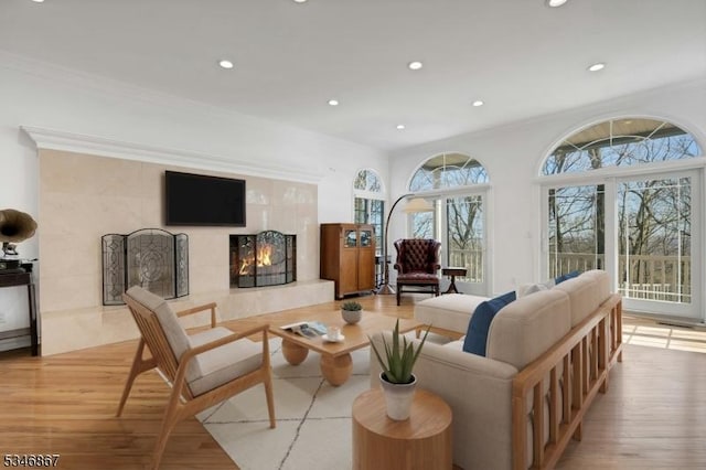 living room with recessed lighting, light wood-style floors, ornamental molding, and a premium fireplace