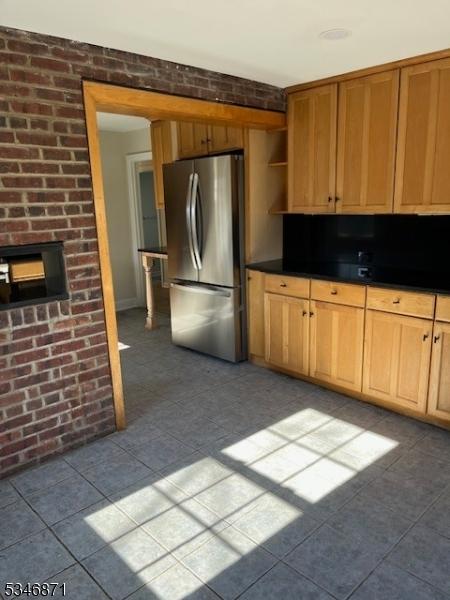 kitchen featuring open shelves, dark countertops, brick wall, freestanding refrigerator, and a fireplace