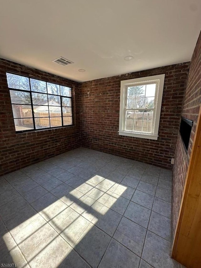 spare room featuring plenty of natural light, brick wall, and visible vents