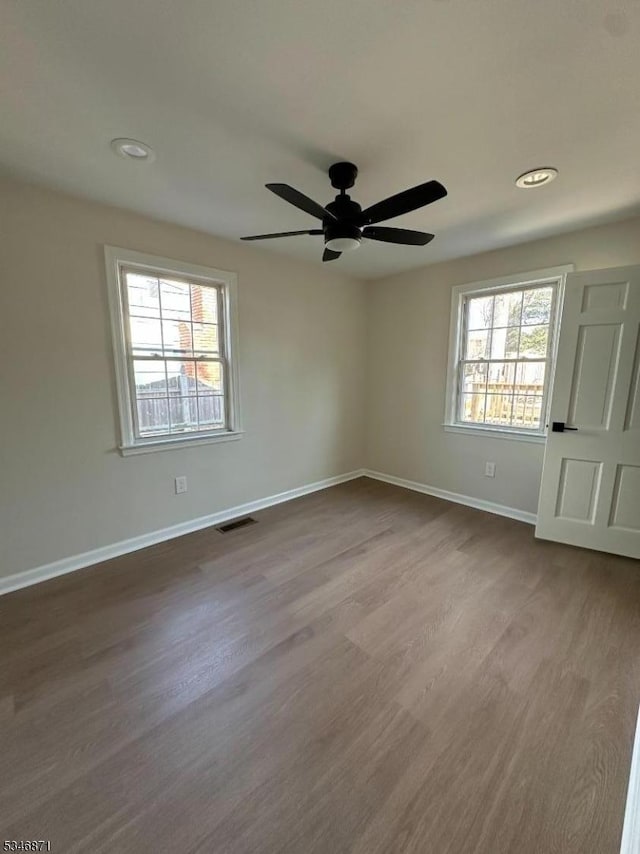 spare room with baseboards, dark wood-style floors, visible vents, and a ceiling fan