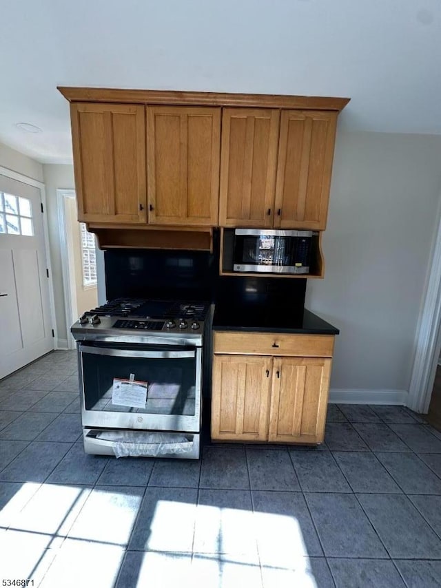 kitchen with dark tile patterned floors, baseboards, dark countertops, appliances with stainless steel finishes, and brown cabinetry
