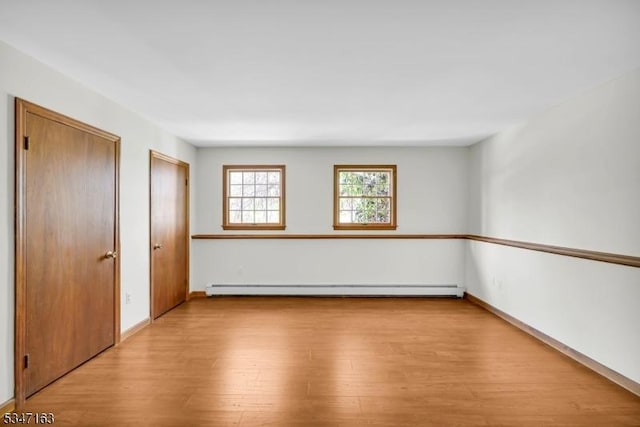 empty room with baseboards, baseboard heating, and light wood-type flooring
