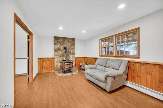 interior space featuring a wood stove, wooden walls, light wood-type flooring, a baseboard heating unit, and a wainscoted wall