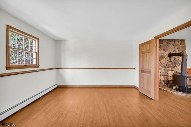spare room featuring baseboards, a wood stove, a baseboard heating unit, and wood finished floors