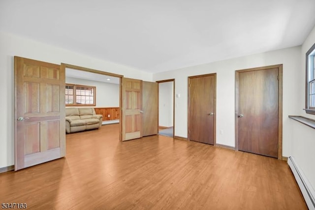 unfurnished bedroom with multiple closets, a baseboard heating unit, and light wood finished floors