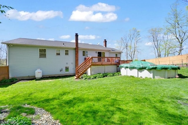 rear view of house featuring fence, a deck, stairway, a chimney, and a lawn